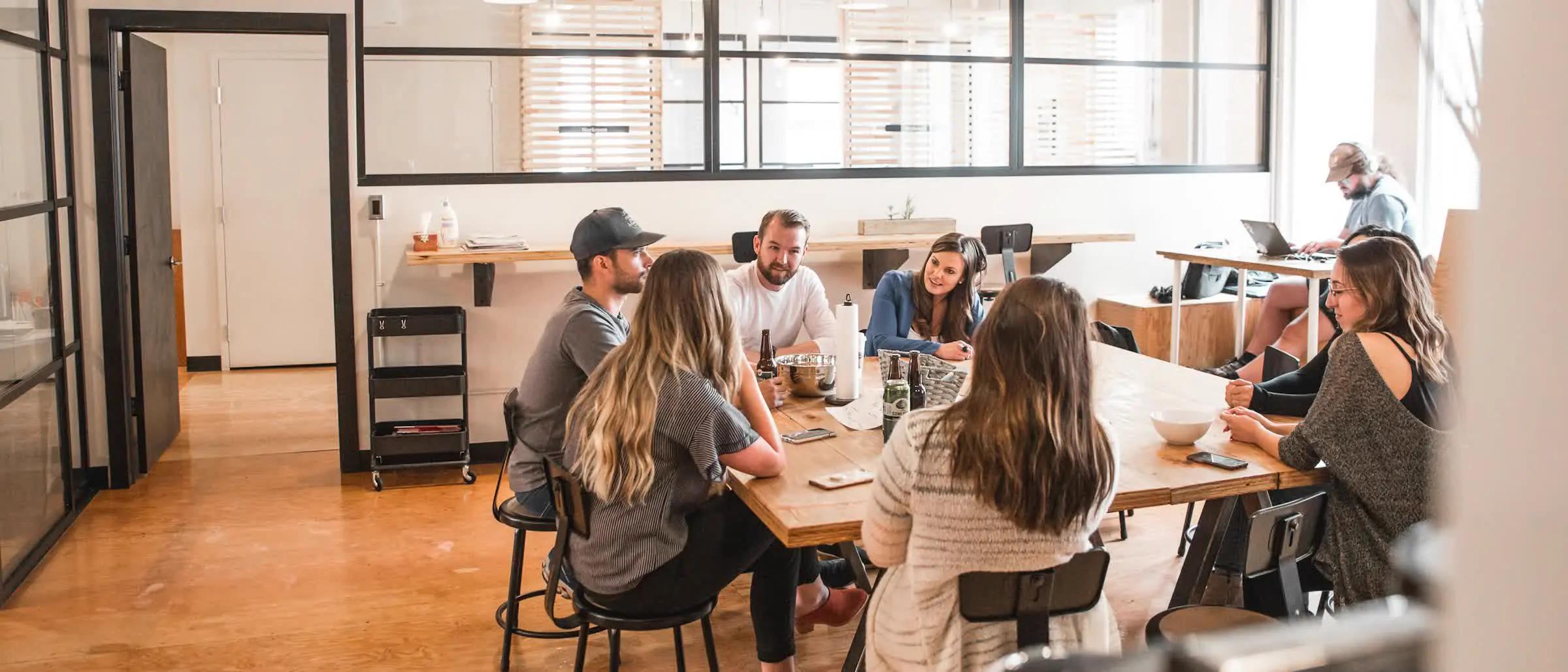 A group of people talking around a long table in a bright open workspace